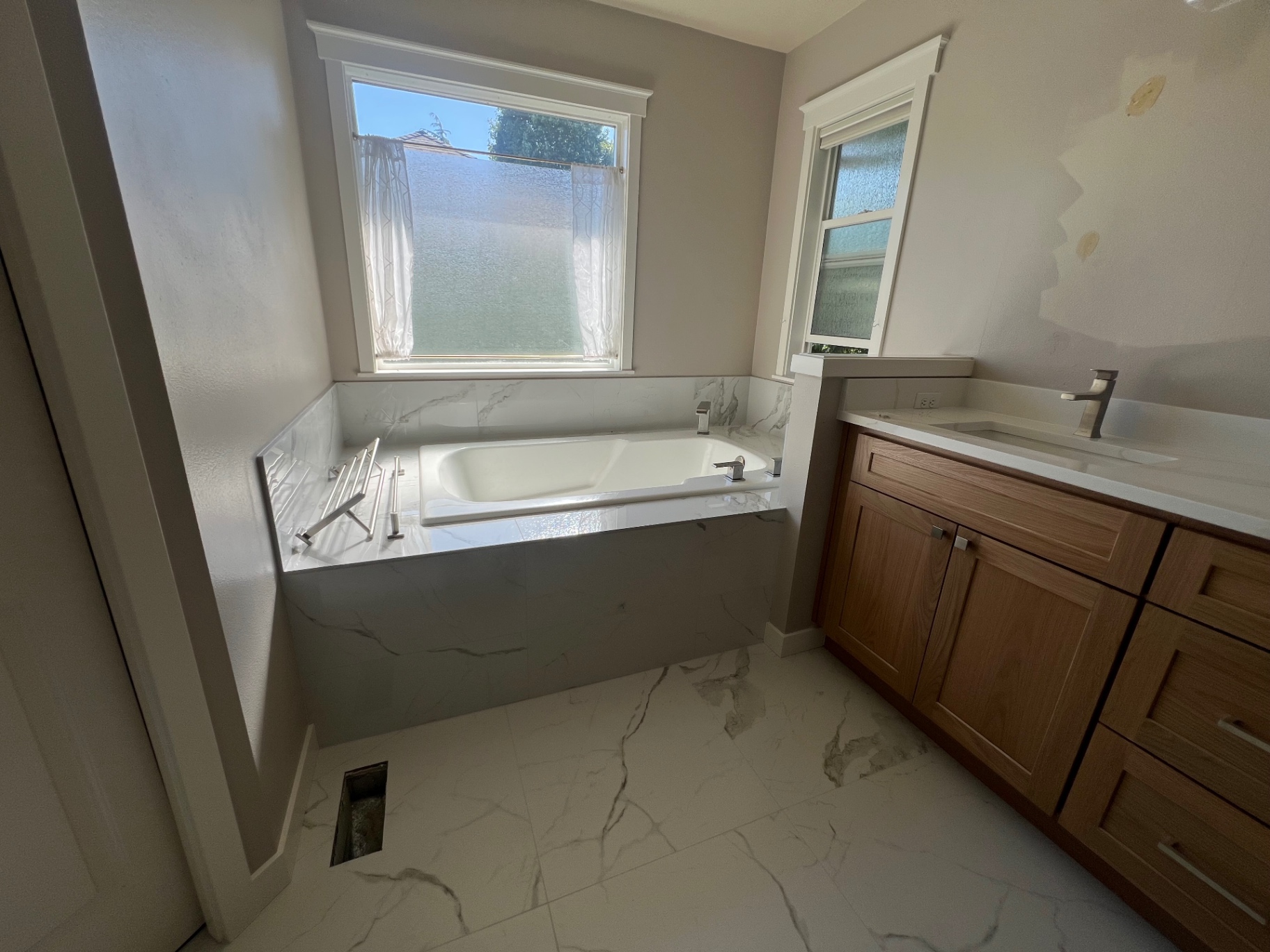 After: large-format marble-look porcelain tile tub surround and matching floor, white oak shaker vanity and quartz counter — completed by NW Home Remodel Pros in West Seattle.